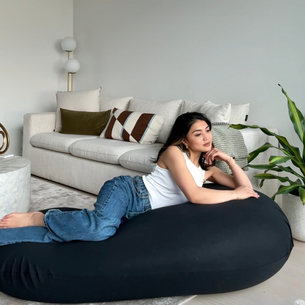 Woman lying on a black bean bag in a living room with a couch and plants.