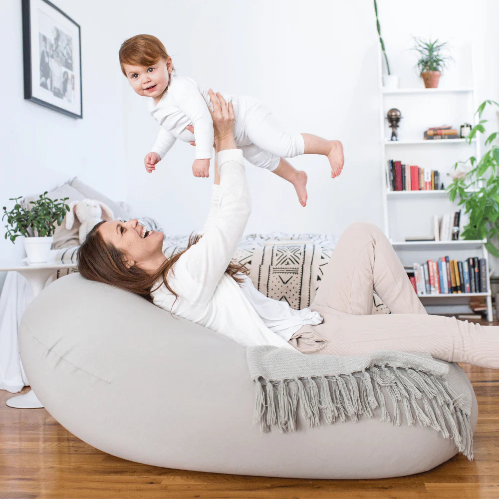 Woman lying on a bean bag chair with a child in a living room setting.