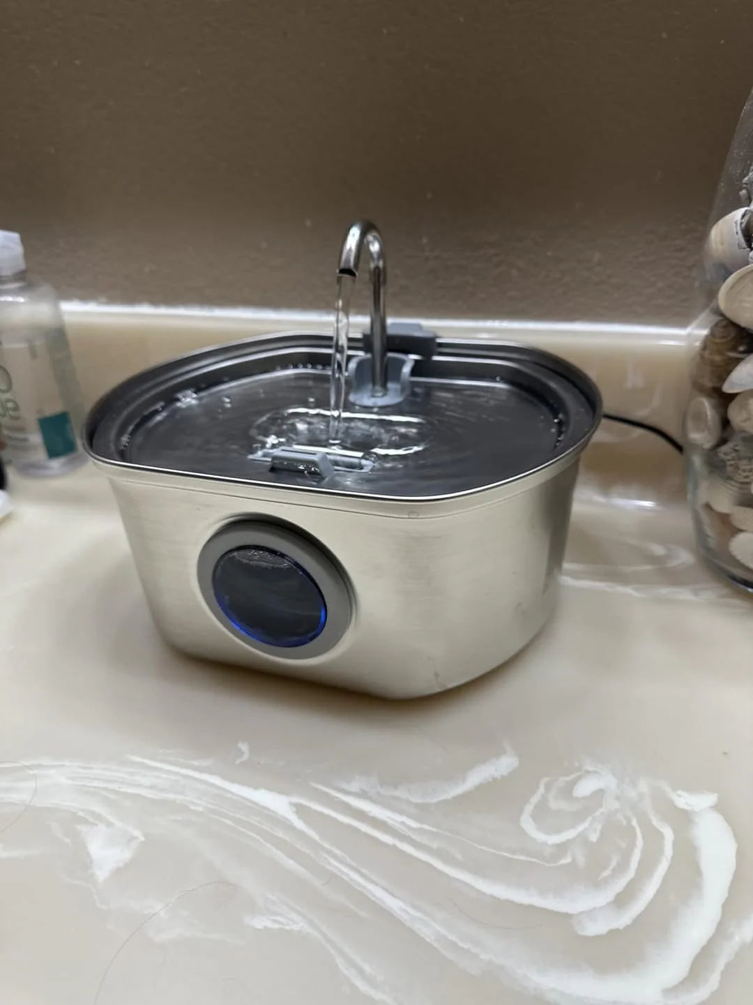 Metal water dispenser on a countertop with a brown wall in the background
