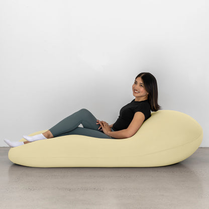 Woman sitting on a light yellow bean bag chair against a white wall.