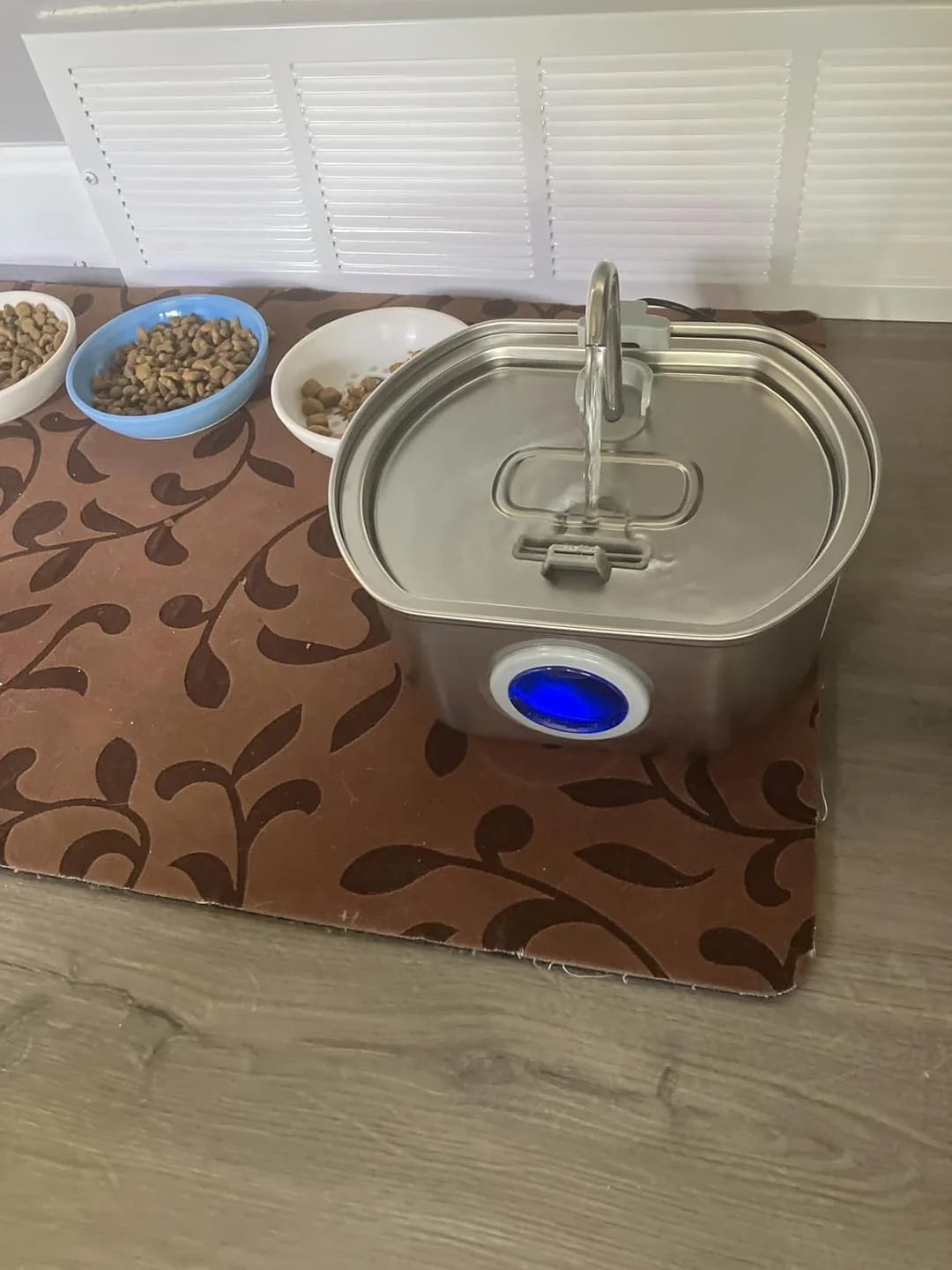 Pet water dispenser with a brown patterned mat on a wooden floor