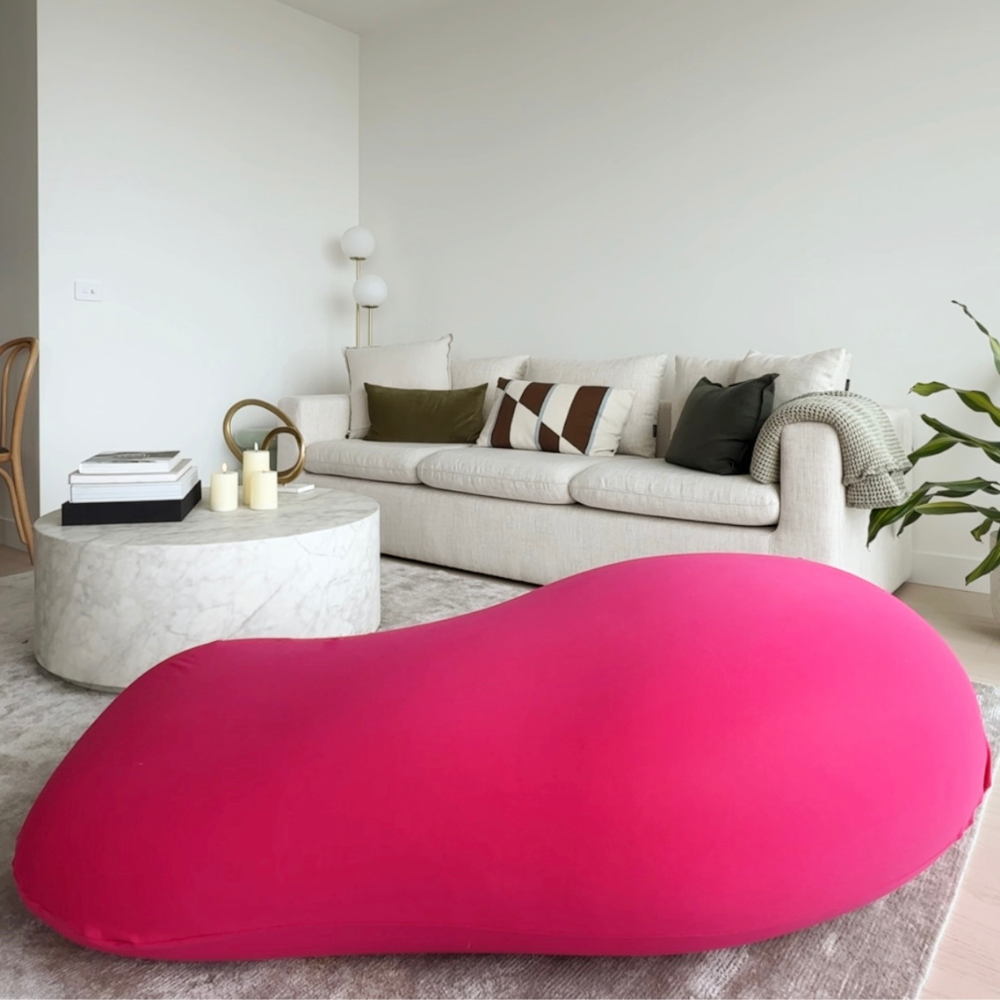 Pink bean bag chair in a living room with a white sofa and decor.