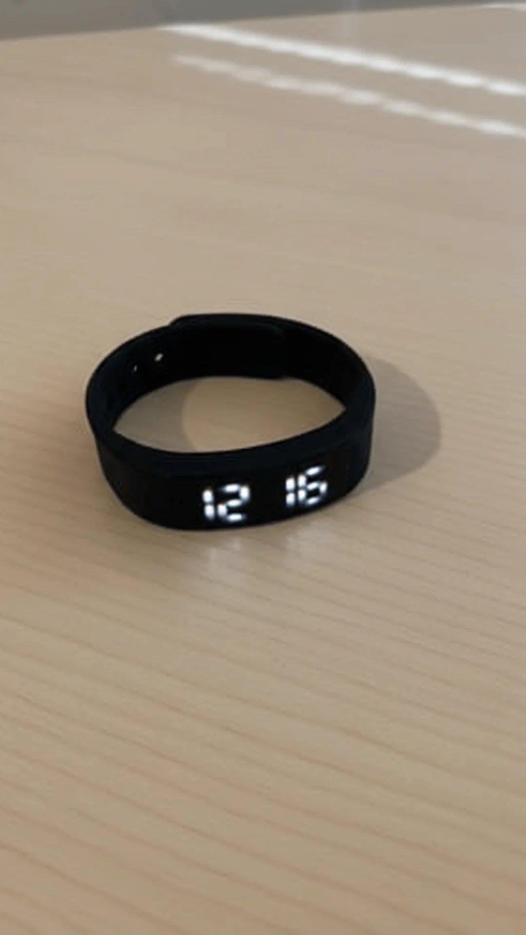 Black digital wristband displaying the time '12:15' on a beige surface.